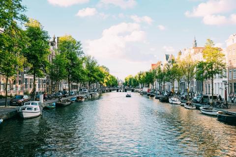 A canal in Amsterdam with buildings, trees, and moored boats on either side